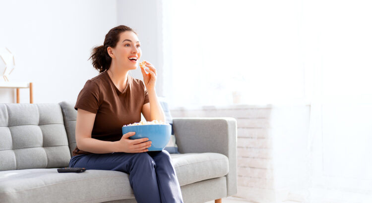 mulher assistindo tv para treinar inglêse comendo pipoca